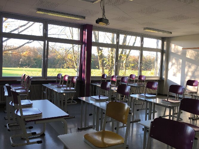 Das Foto zeigt einen typischen Klassenraum der Jahrgangsstufe 5 mit Sicht auf die grüne Umgebung der Schule und mit Verweis auf die digitale Ausstattung unserer Schule nach unserem Profilgedanken 